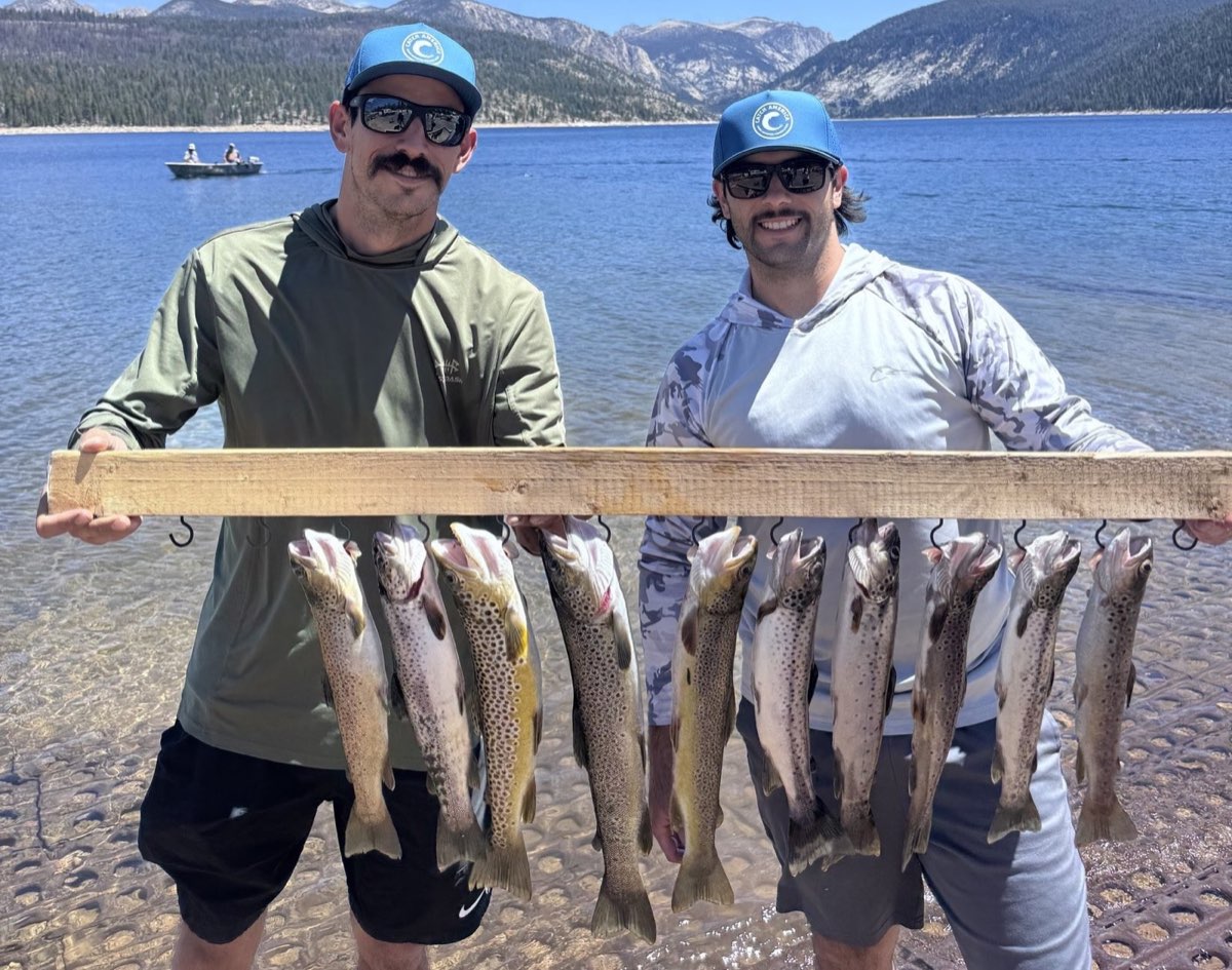 Two anglers in Catch America hats holding a stringer of trout at a mountain lake